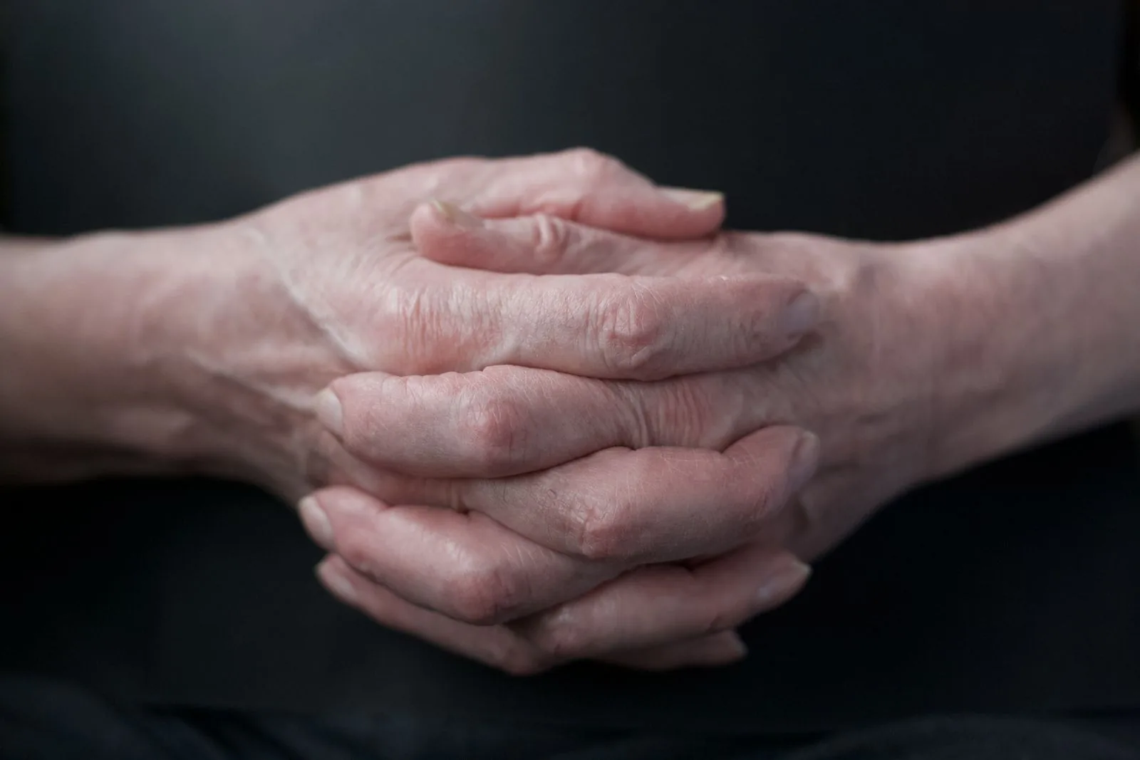 Close-up of an elderly person's folded hands resting in their lap