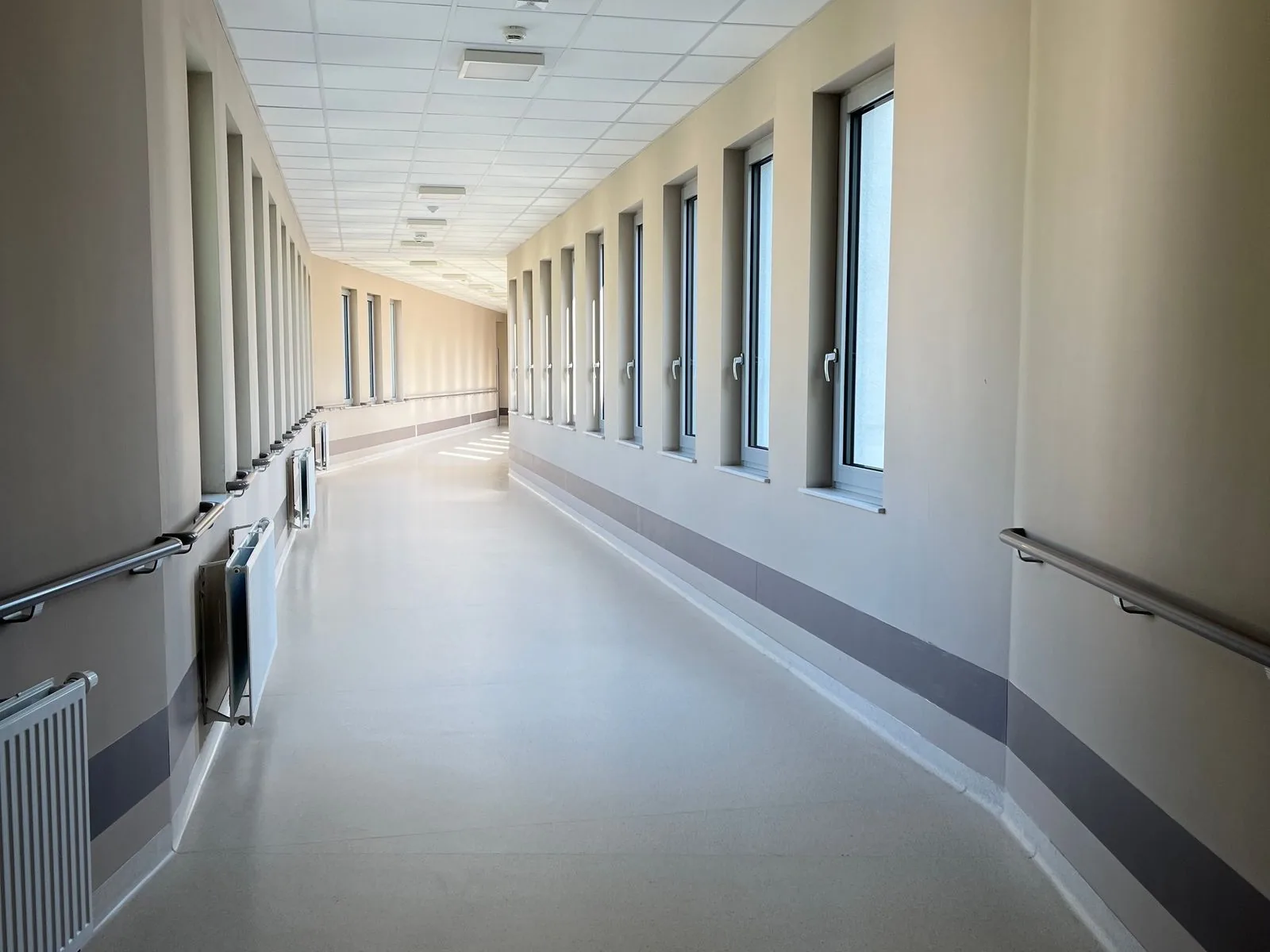 An empty, daylit corridor in a long-term care facility, lined with grab rails