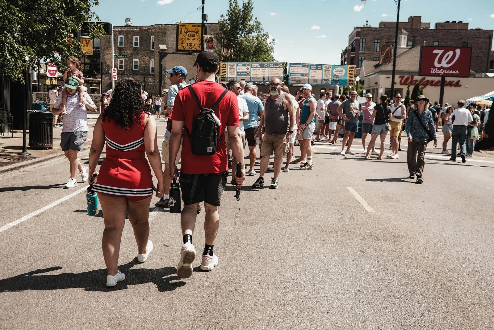 A diverse crowd of everyday people walking together down a sunlit city street